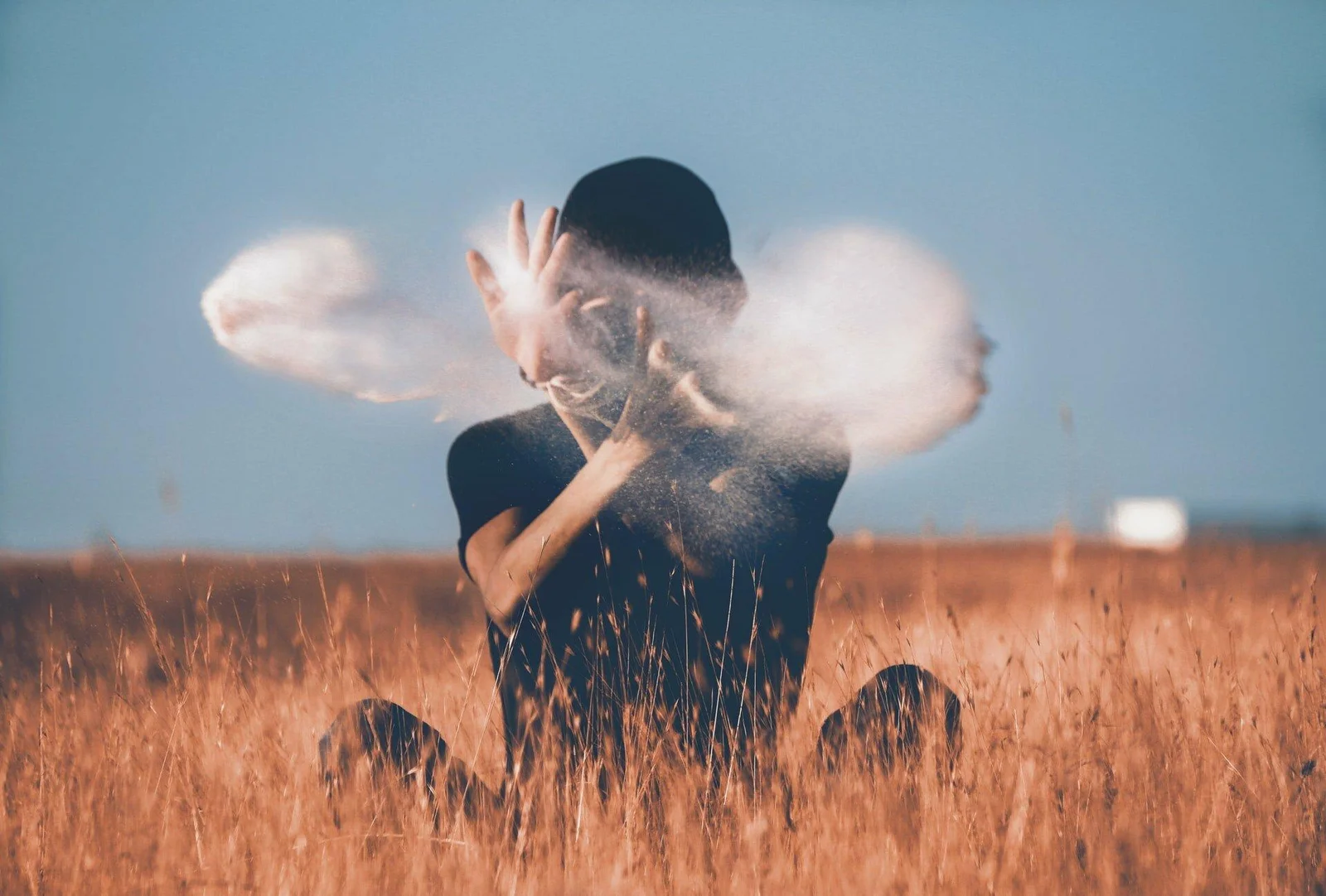 A person kneeling in an open field, dust caught in the light around them